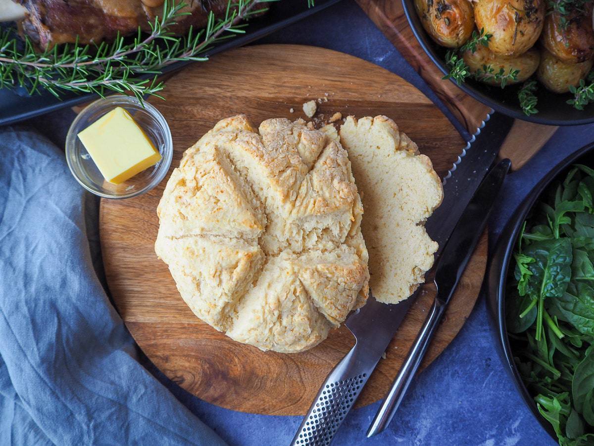 Easy no-knead Damper bread on a round wooden cutting board next to a butter.