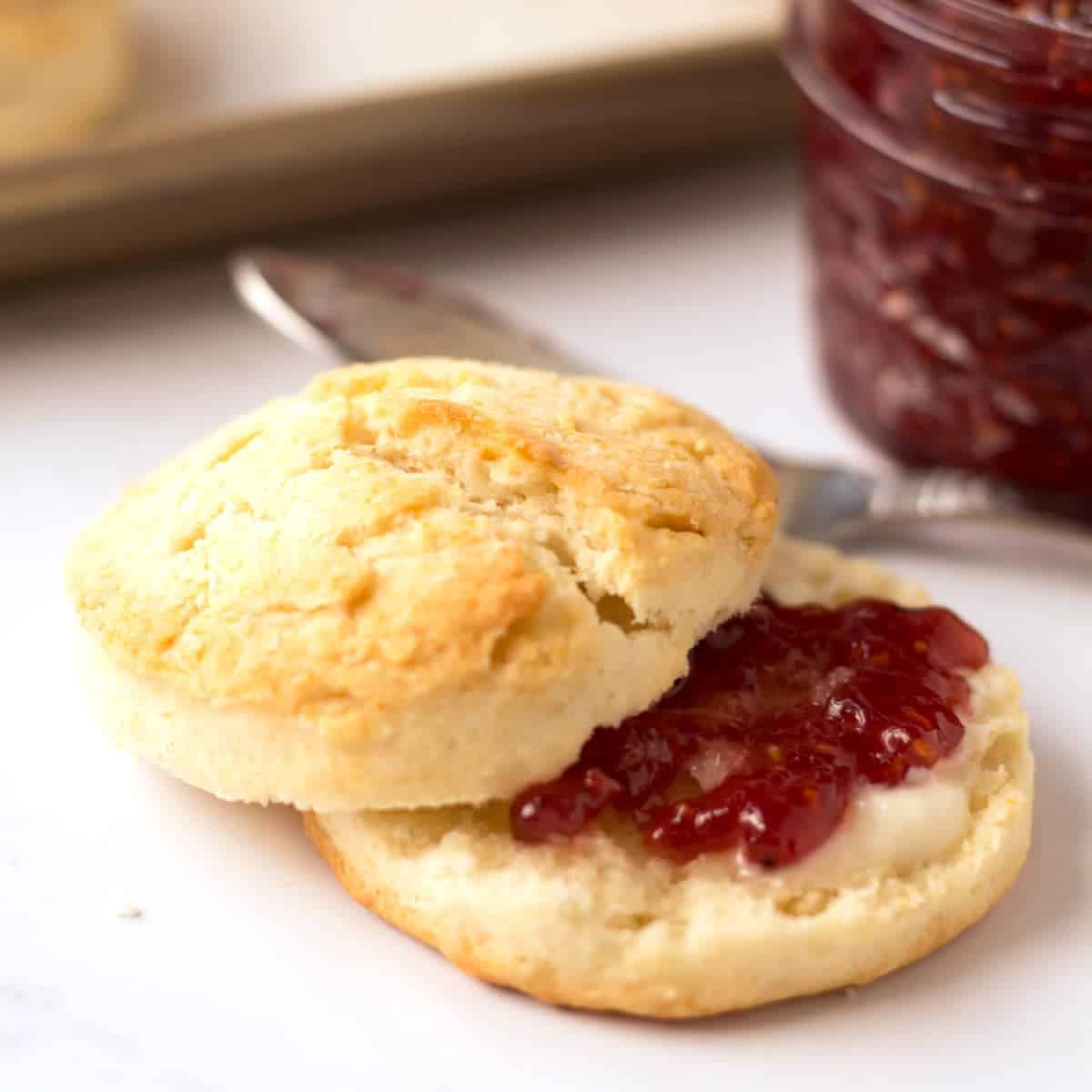A biscuit with jam on it next to a jar of jam.