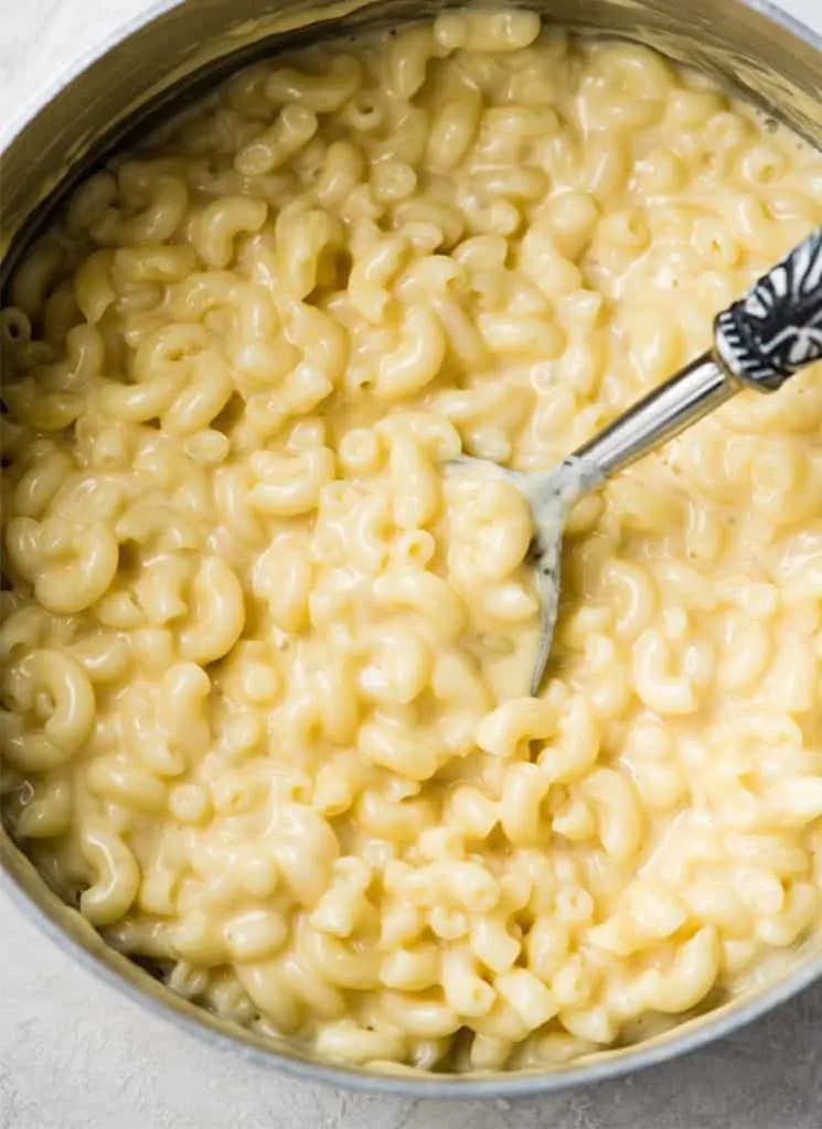 Homemade macaroni and cheese in a pot with a serving spoon.