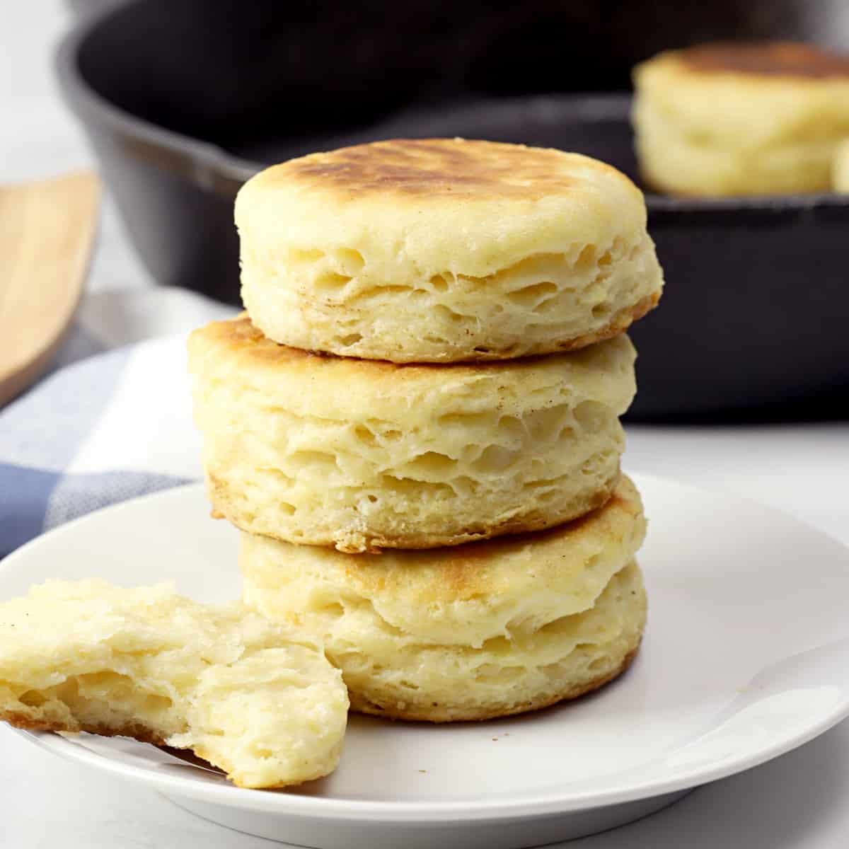 A stack of biscuits on a white plate next to a skillet.