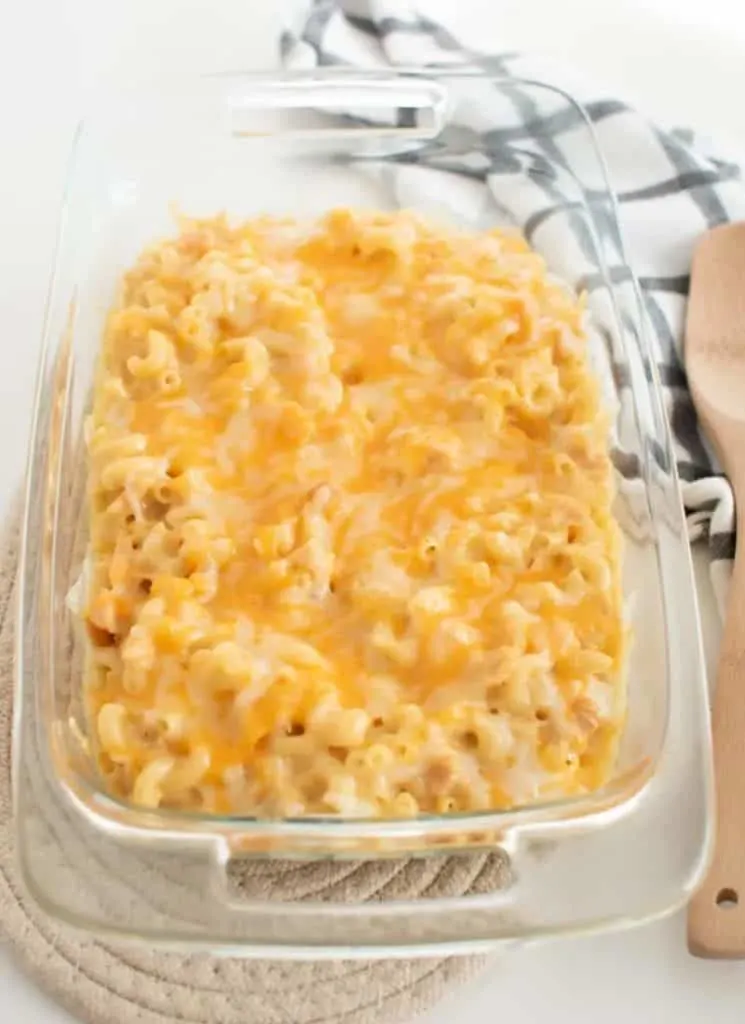 Baked macaroni and cheese in a glass dish with a wooden spoon.