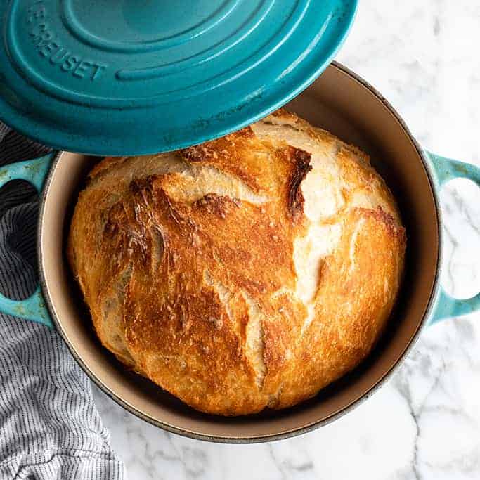 A blue Dutch oven filled with freshly baked no-knead bread.