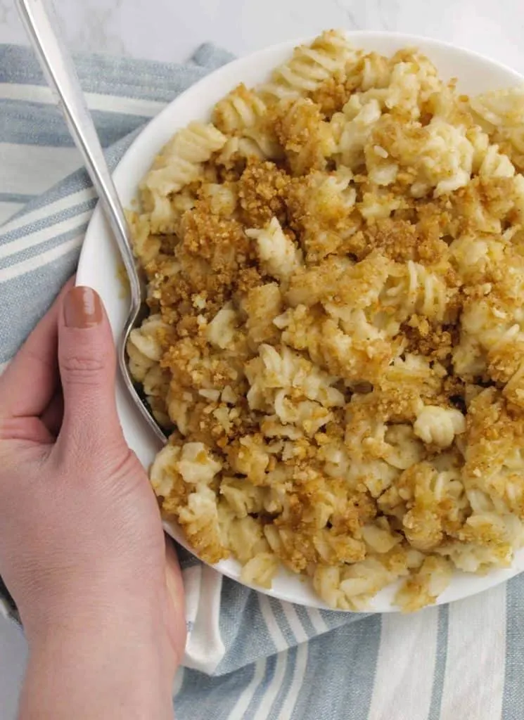 Woman's hand holding dish of easy baked mac and cheese recipe.