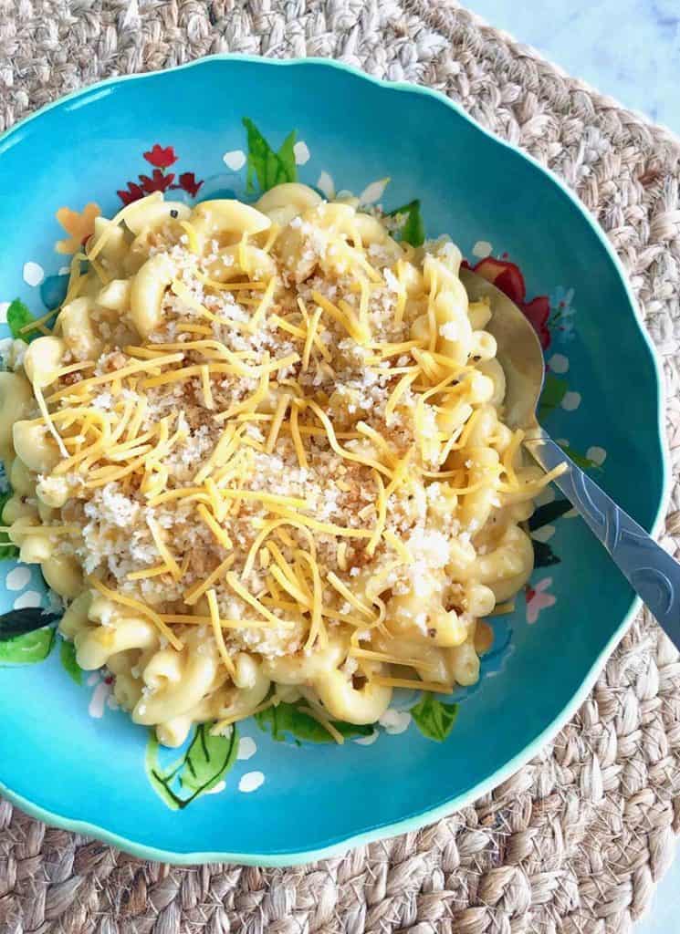 Stovetop macaroni and cheese with bread crumbs and shredded cheese on a blue plate.