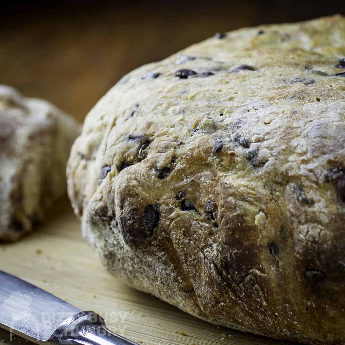 A no-knead bread loaf on a cutting board with a knife.