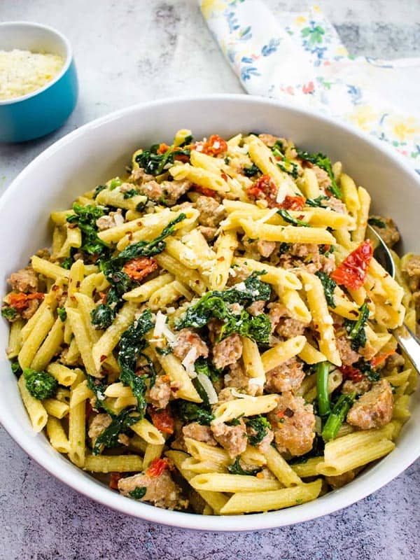 Sausage pasta recipe in a white bowl on the table with a serving spoon.
