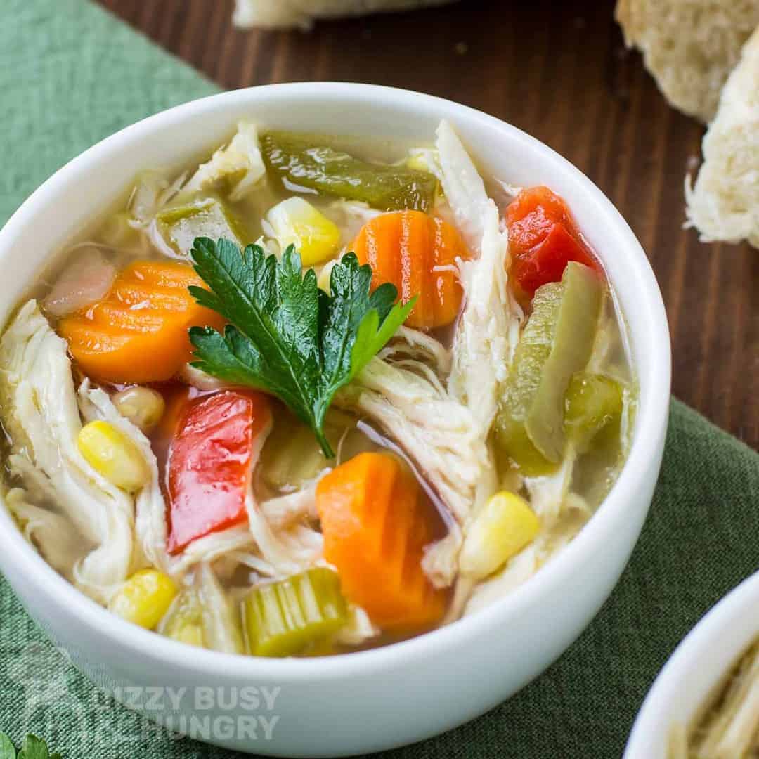 A bowl of chicken noodle soup with carrots and corn.