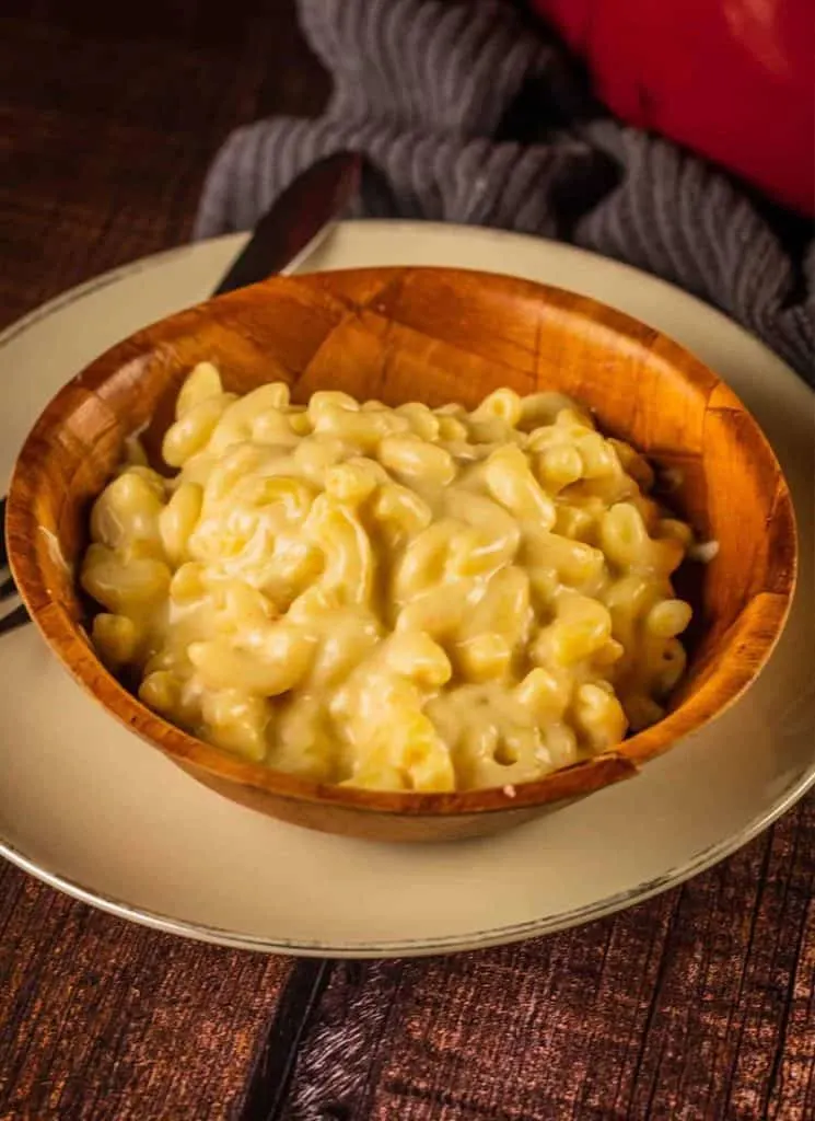 White cheddar macaroni and cheese in a wooden bowl on a plate.