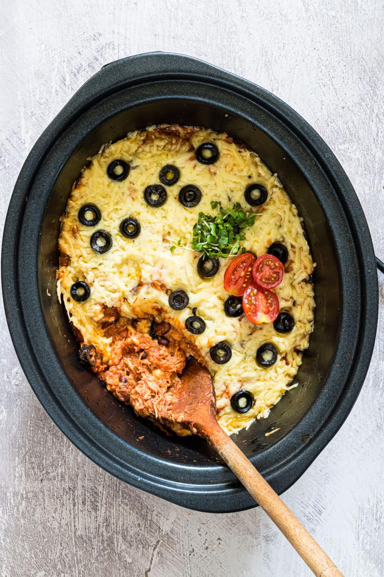 Easy slow cooker chicken enchiladas casserole with a wooden spoon.
