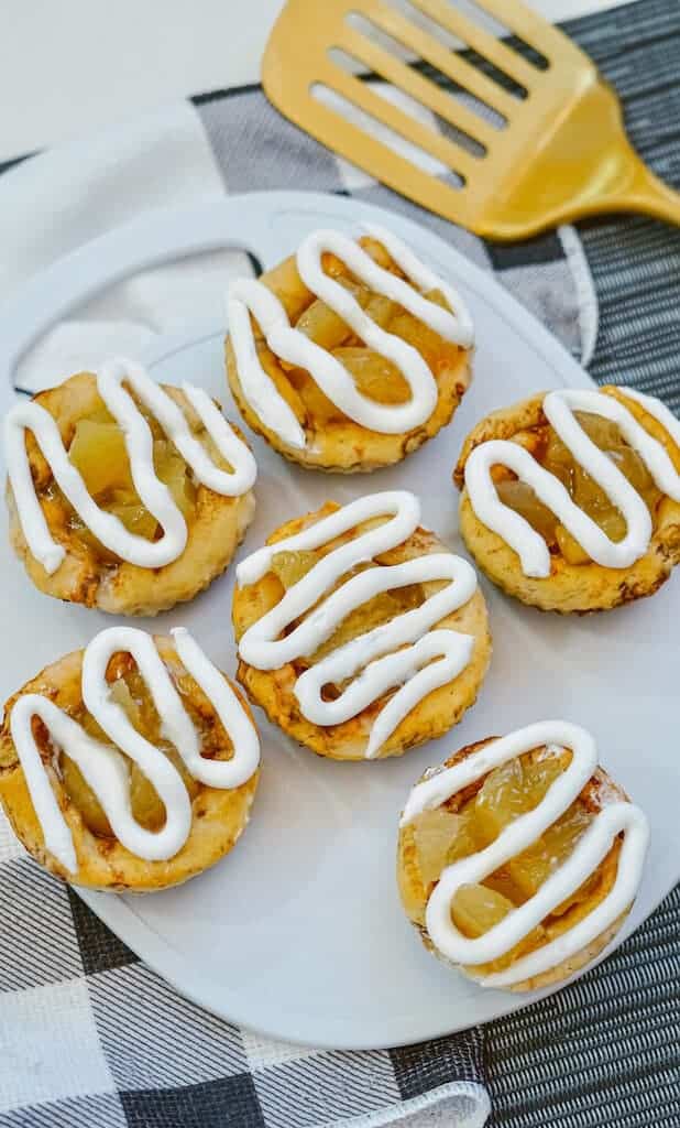 Six easy apple pie rolls with icing on a white plate.
