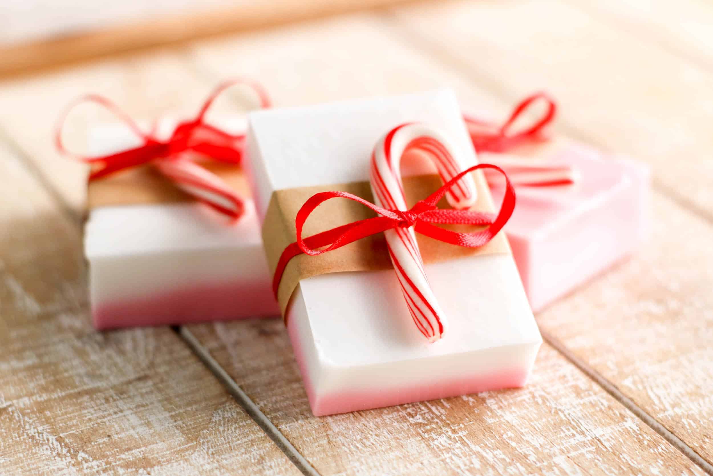 Three red and white layered bar soaps each tied to.a candy cane using a pink ribbon.
