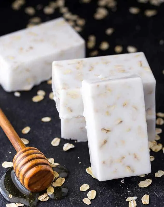 Three white oats soap bars next to a honey dipper.