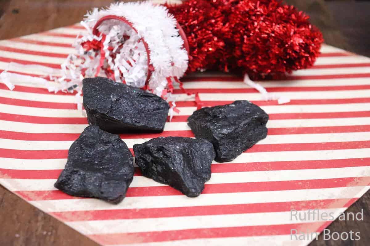 Four pieces of coal soap on top of a red and white striped paper next to red ribbon.