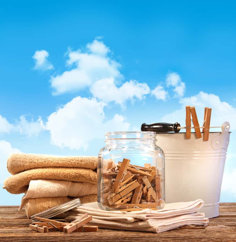 Wooden clothes pins in a bucket and a glass jar with brown towels at the background.