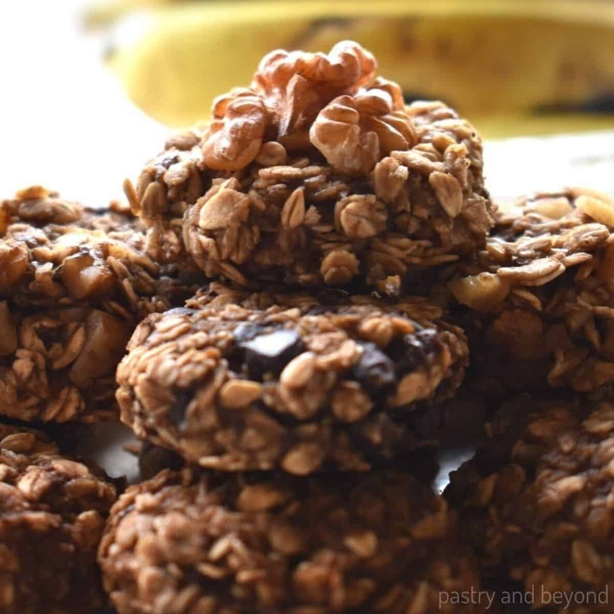 A close up photo of oatmeal chocolate cookies with the view of a banana on the background.