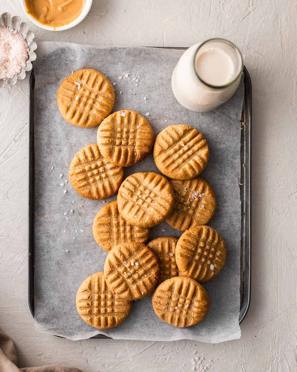 A baking tray filled with peanut butter cookies and a glass of milk.