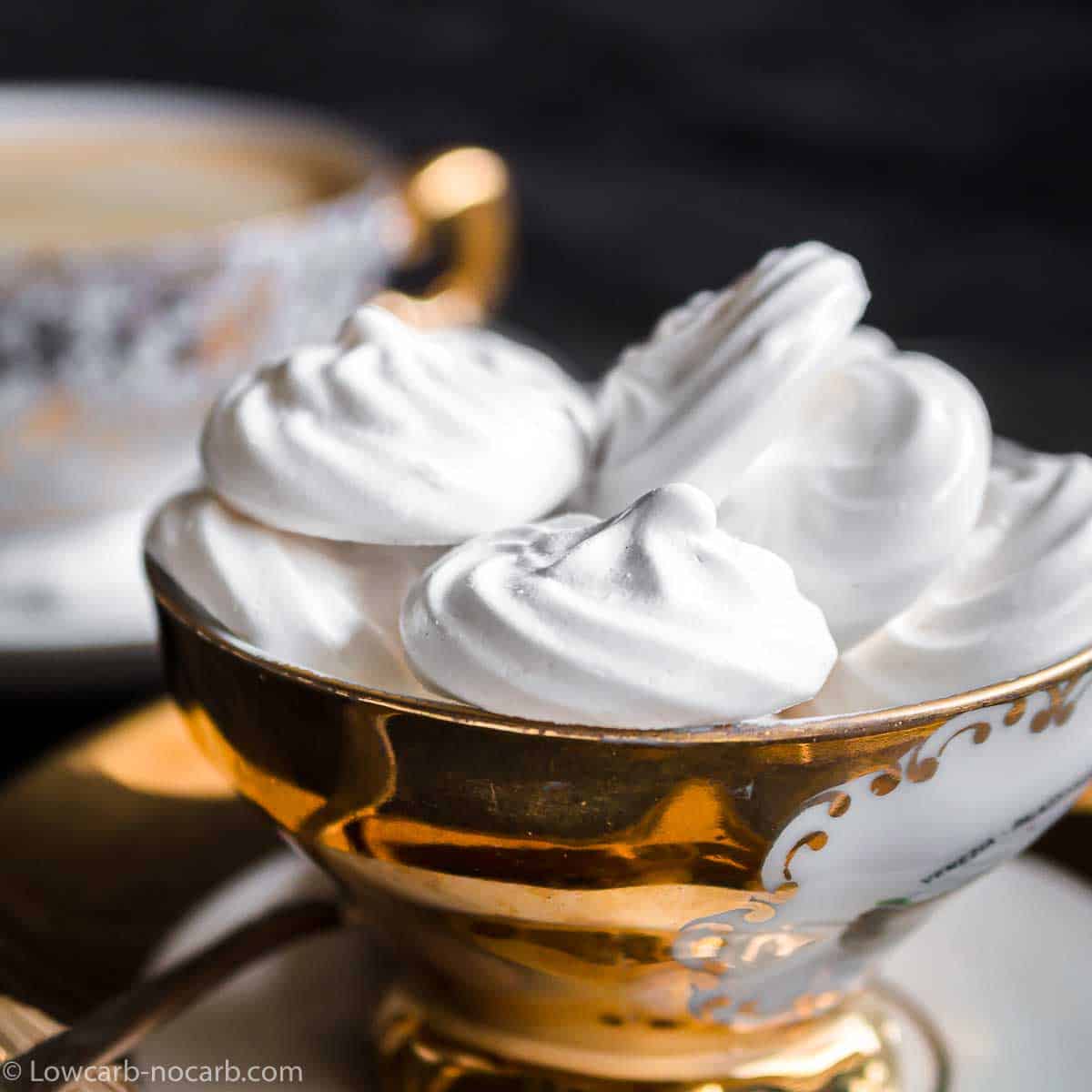White meringue cookies in a gold bowl next to a coffee cup.