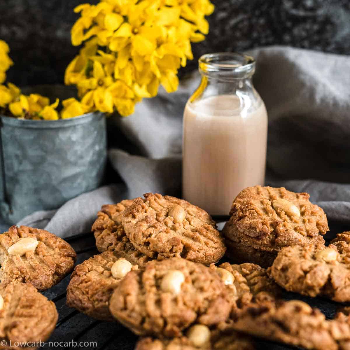 Peanut butter cookies with nuts next to a jar of milk and a vase with yellow flowers.