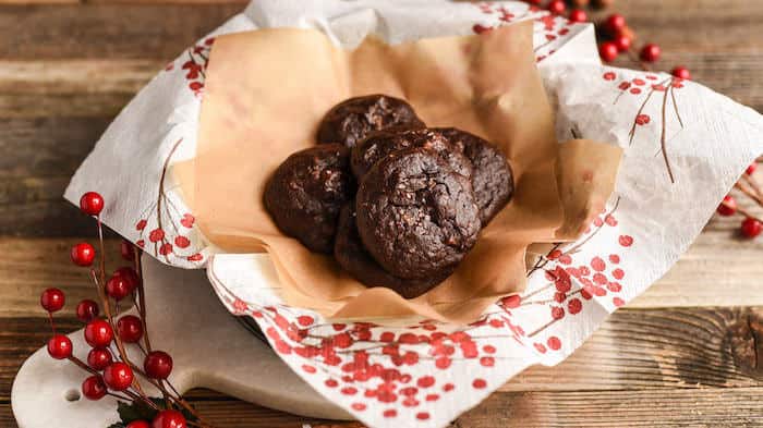 Chocolate cookies in a plate with brown parchment paper and white parchment paper with holly berries design.
