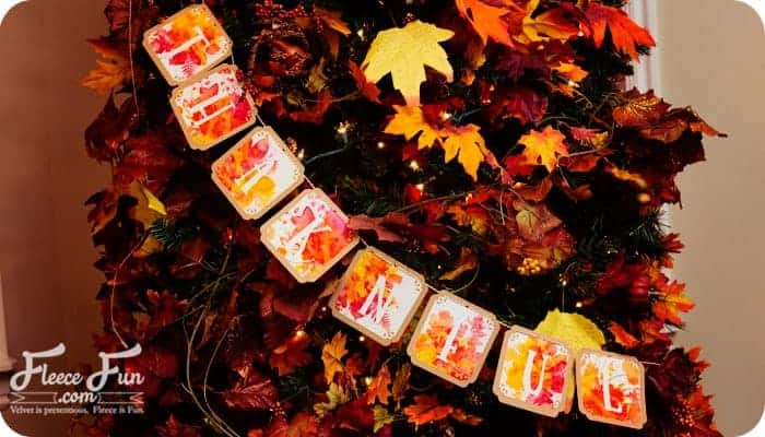Thankful banner hanging on an indoor display tree with red and yellow fall leaves.