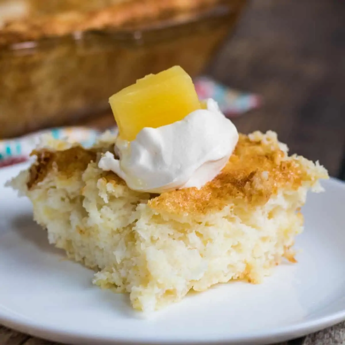 A slice of pineapple sponge cake with whipped cream on a white plate.