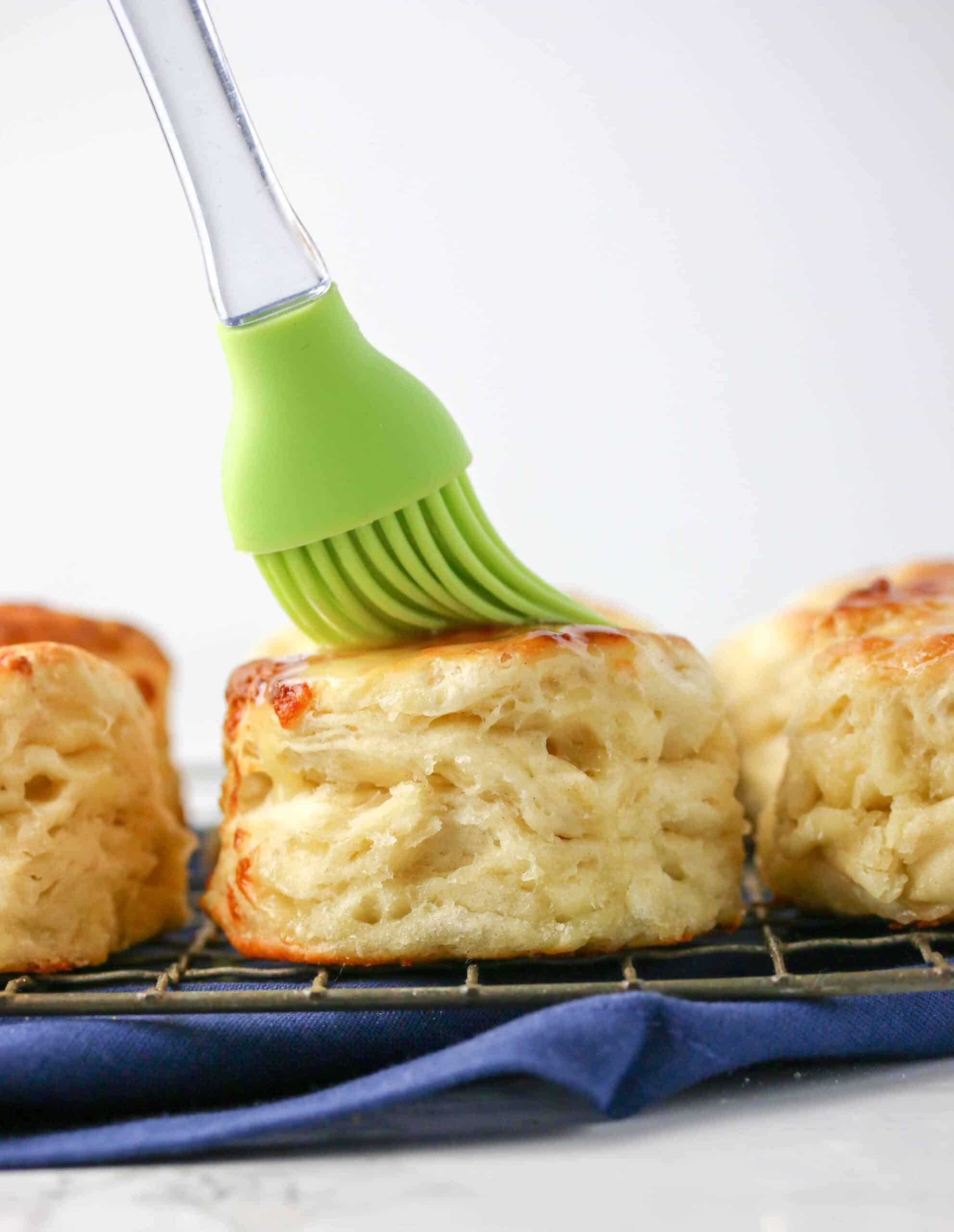 Biscuits on a cooling rack with one of them being brushed with butter on top.