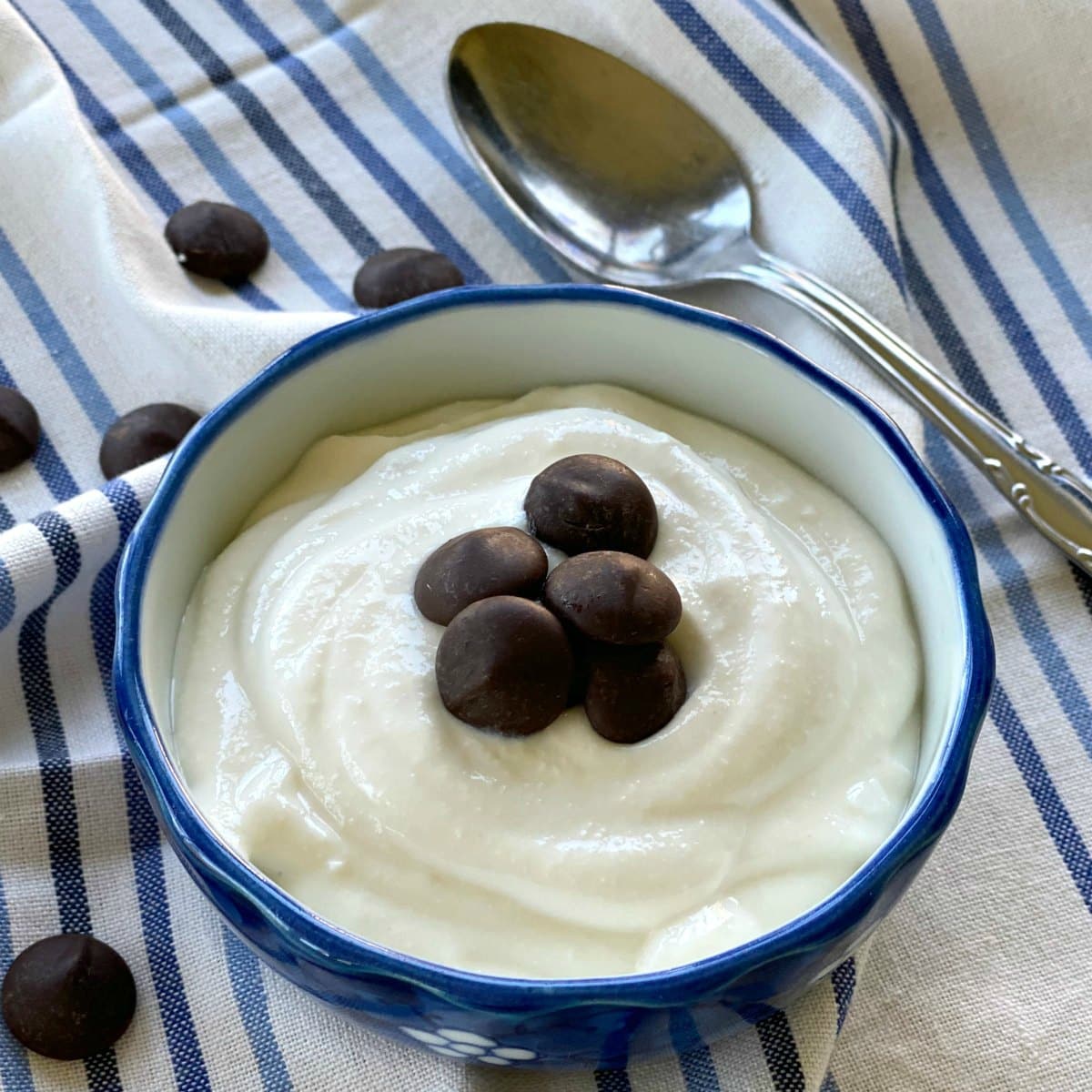 Whipped cottage cheese dessert garnished with chocolate chips on a blue bowl on top of a white and blue striped cloth.