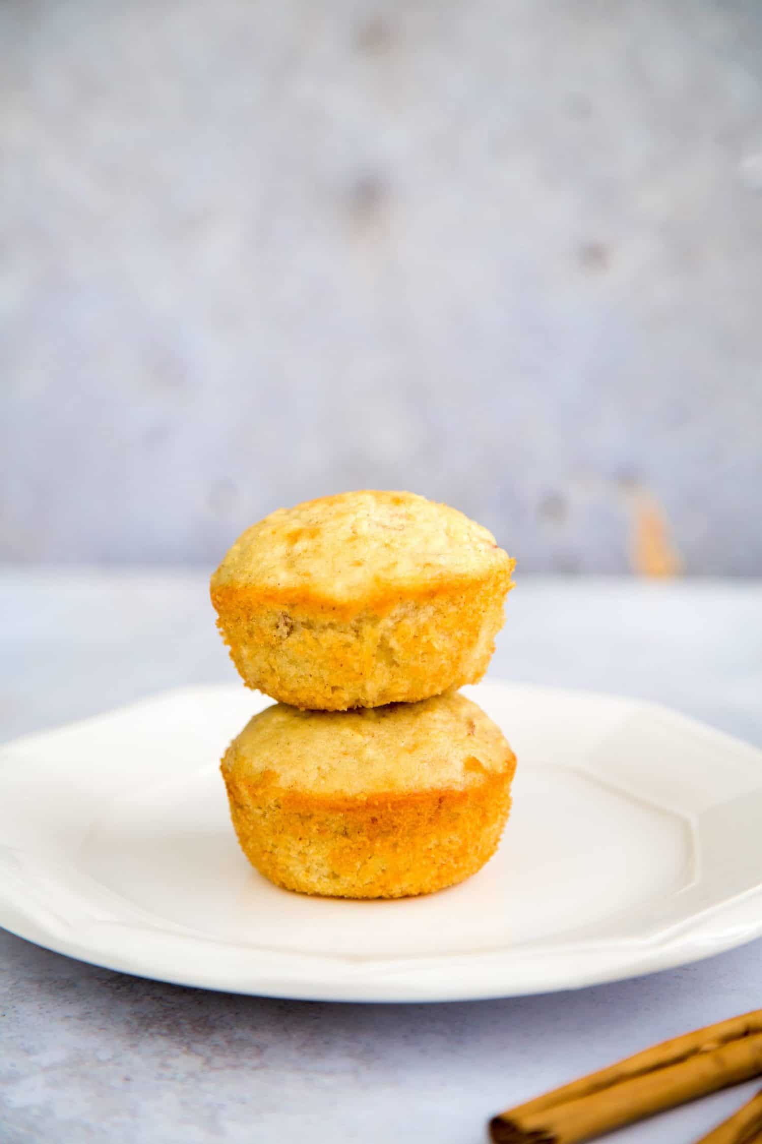 Two apple cinnamon muffins stacked together on a white serving plate.
