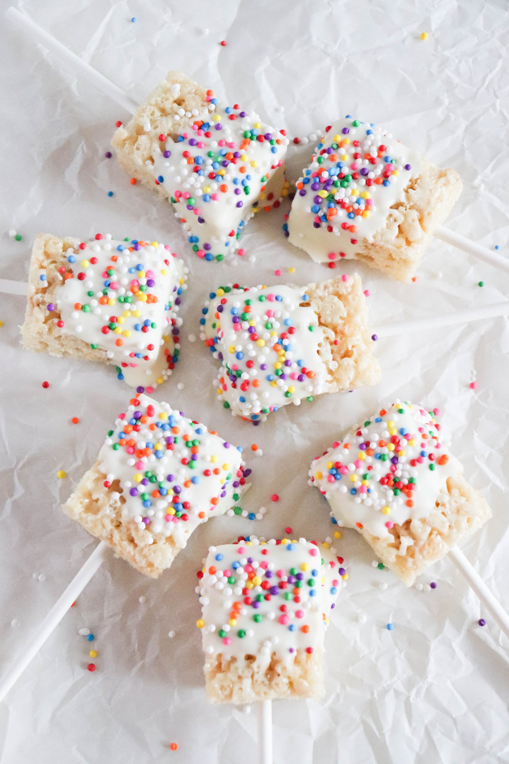 Rice krispie treats on sticks with sprinkles placed on white napkin.