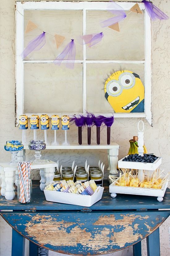 Minion party snack table with the face of a minion decorated on the window on the background.