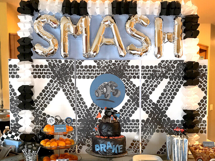 Monster truck-themed party with a snack table with a big wheel cake and "smash" background.