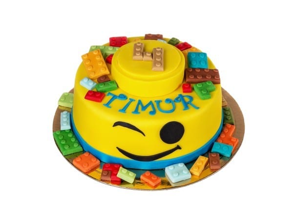 Yellow lego birthday cake with a winking face and lego pieces on top and on the sides of the cake.
