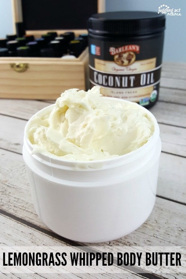 Whipped body butter in white jar. A jar of coconut oil and a wooden box full of essential oils in the background.