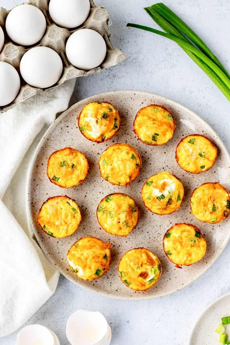 Egg bites arranged on a plate next to a carton of eggs.
