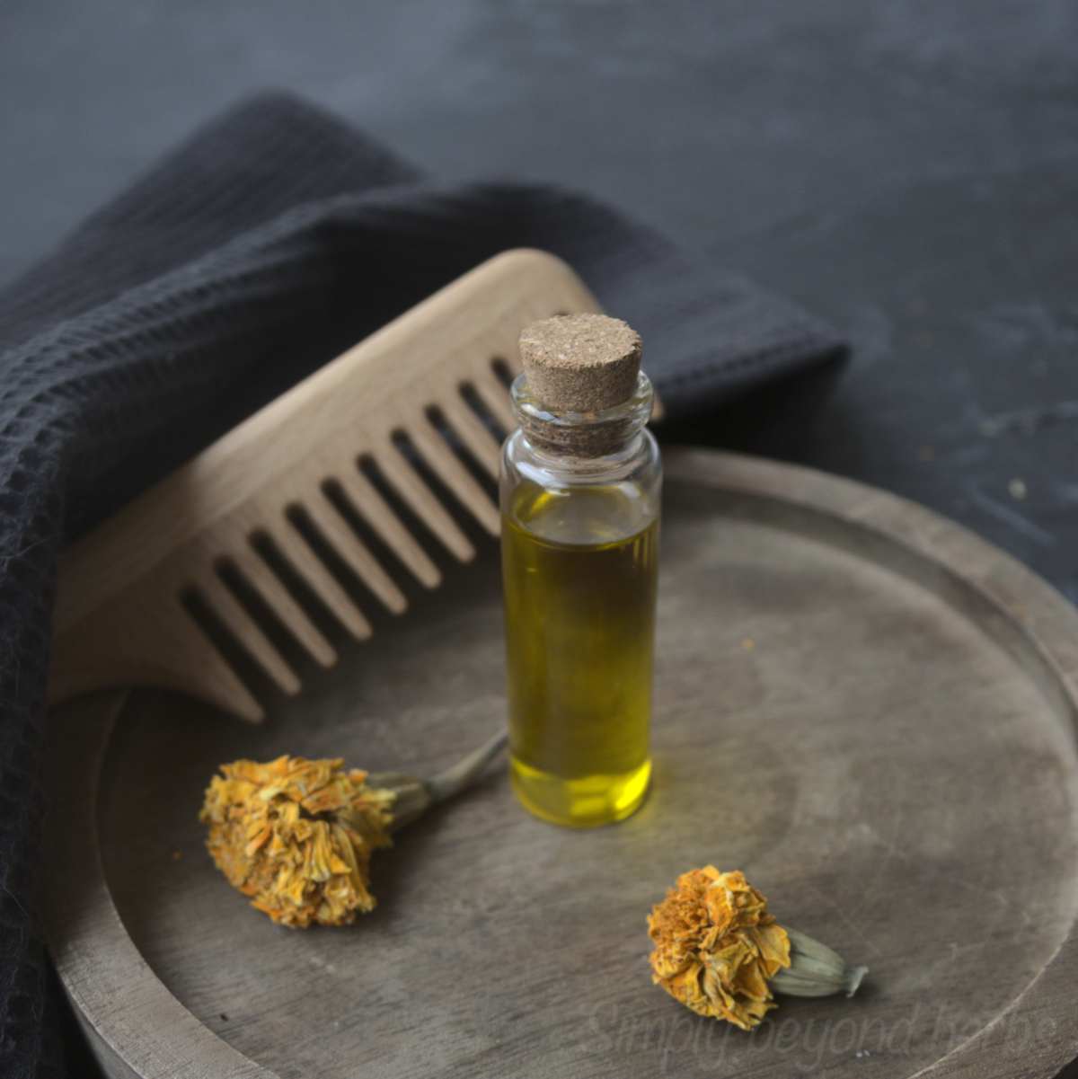 Hair growth oil in a small stopper bottle next to dried calendula flowers and a wooden comb.
