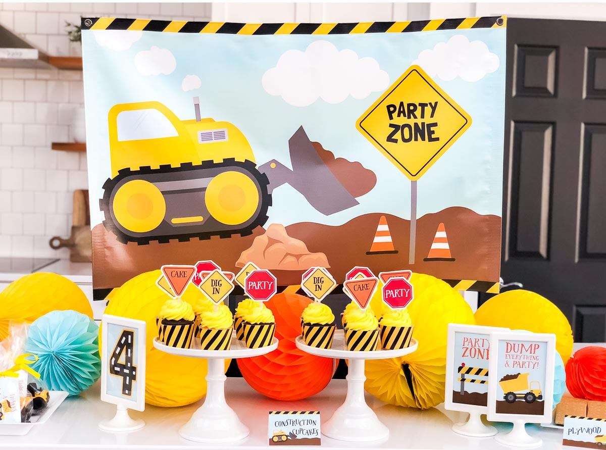 Yellow cupcakes with small flags that say dig in, cake and party in two trays. Construction party zone as background.