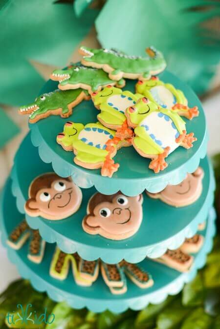 A 3-tier cupcake stand filled with treats that look like frog, crocodile and monkey.
