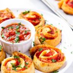Pizza pinwheels rolls with marinara dip on a white serving plate.