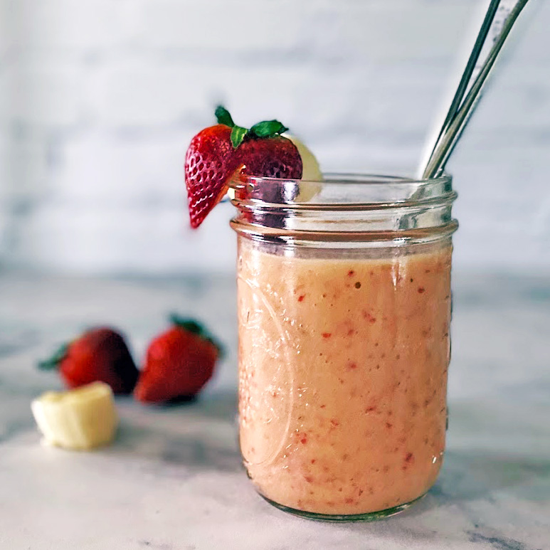 Banana strawberry mango smoothie in a mason jar with strawberry and straw.