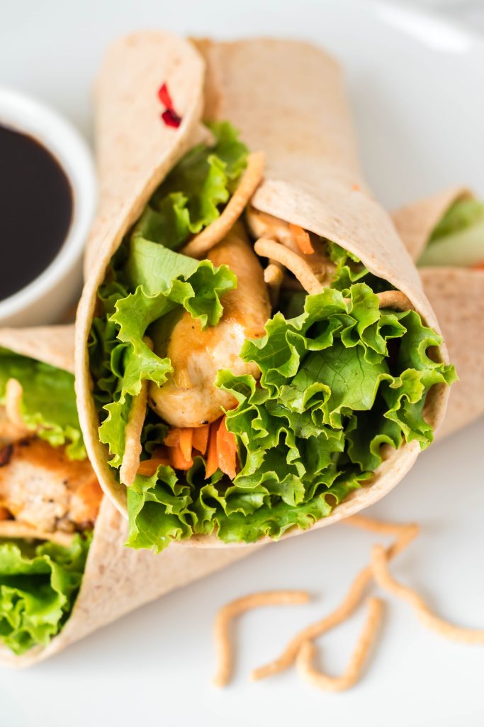 Two chicken asian wraps with dipping sauce in a white plate.