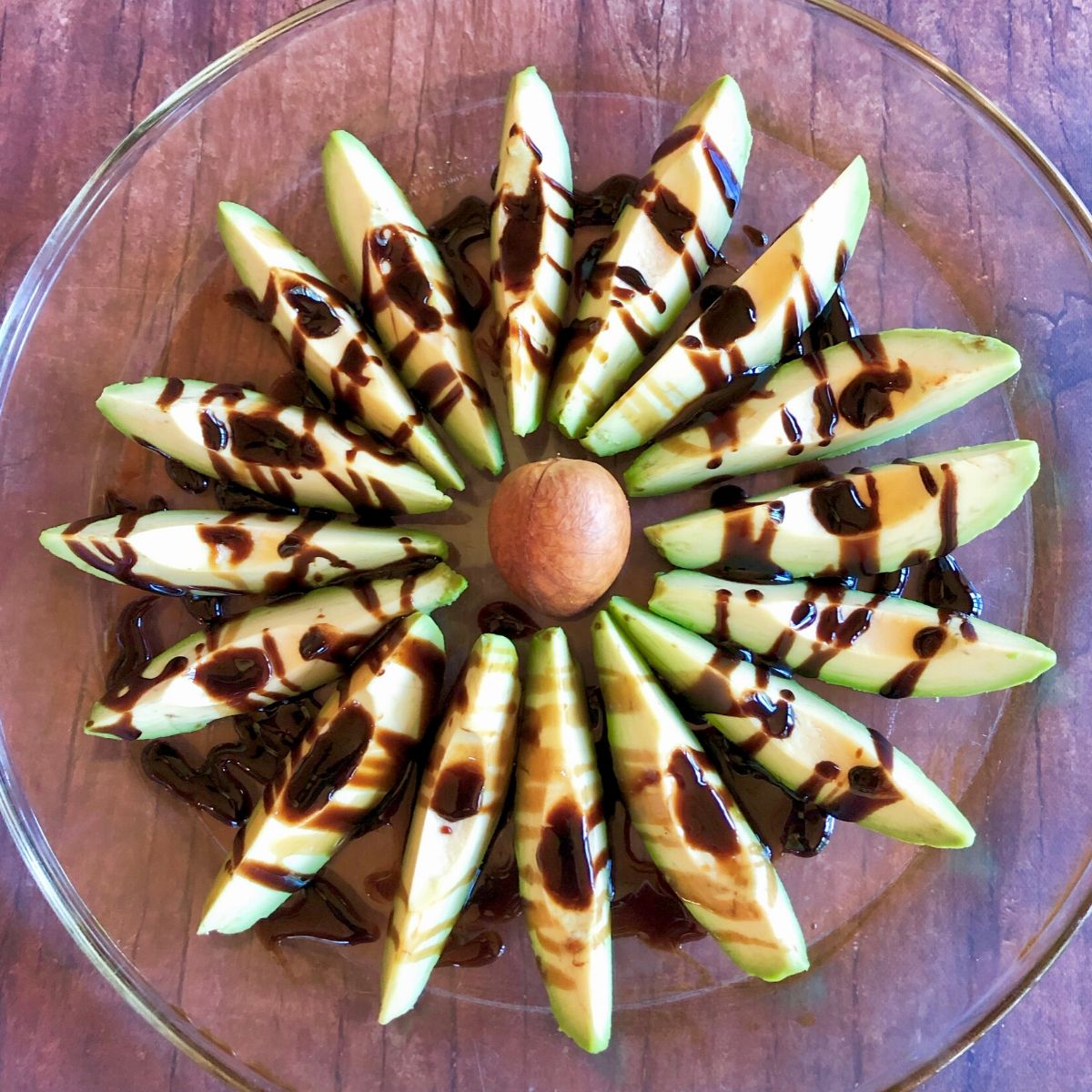 Avocado slices in a circle forming a flower drizzled with balsamic vinegar.