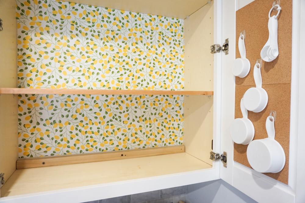 A cabinet with a liner designed in yellow and green with measuring cups and spoons hanging on the cabinet door.