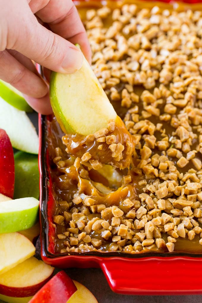 A person holding a slice of green apple dipping it into the caramel apple dip.