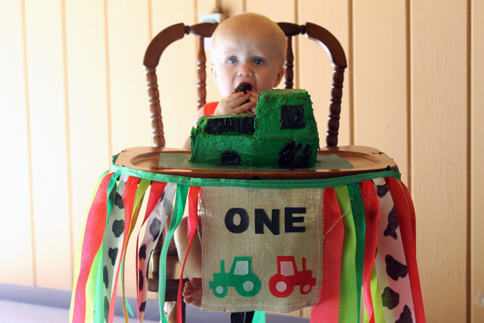 A baby in front of a table with a tractor cake and a one banner with farm theme.