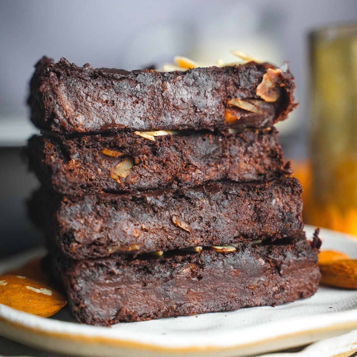 5-ingredient brownies stacked up on a plate with almond nuts.