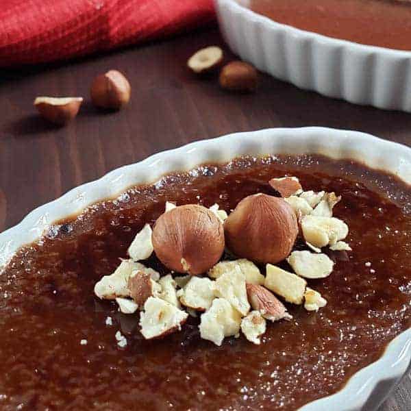 Hazelnut creme brûlée in white dish garnished with whole and crushed hazelnuts.
