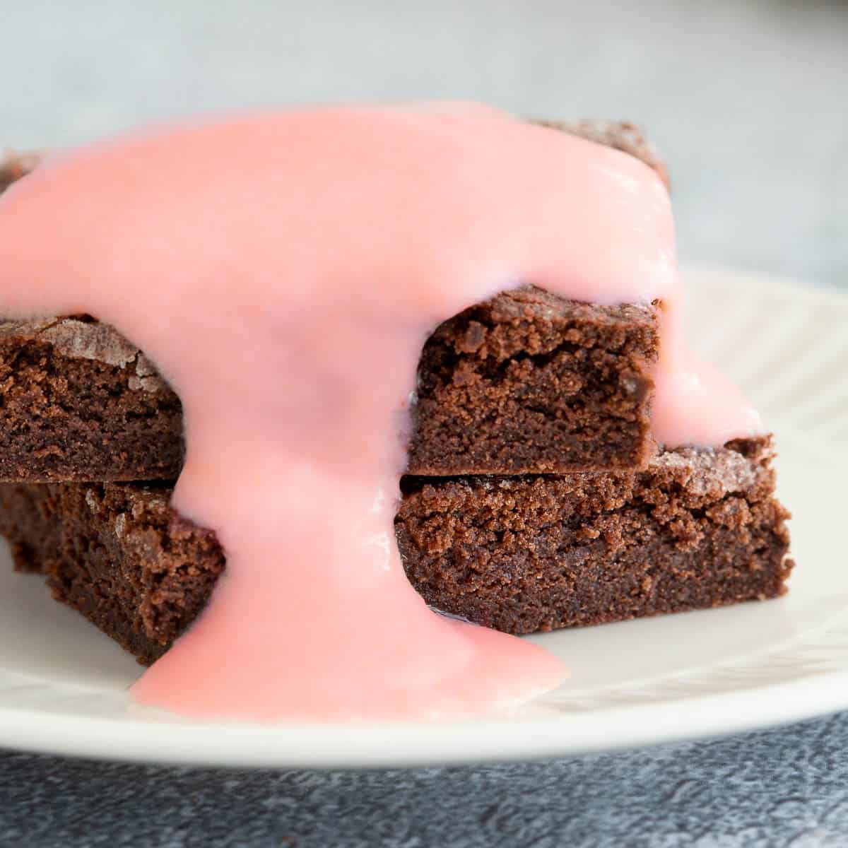 Two chocolate concrete stacked together with pink frosting on a white plate.