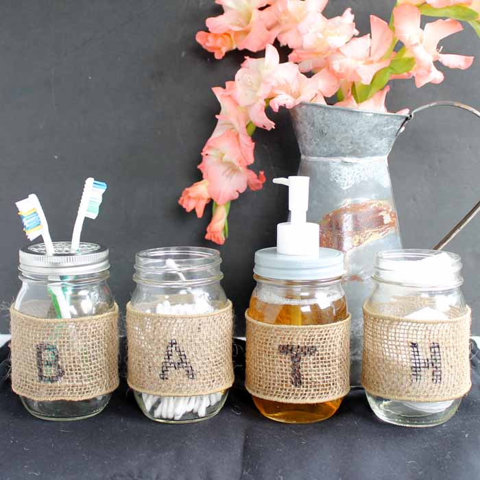 A set of four small mason jars with burlap for bathroom organization.