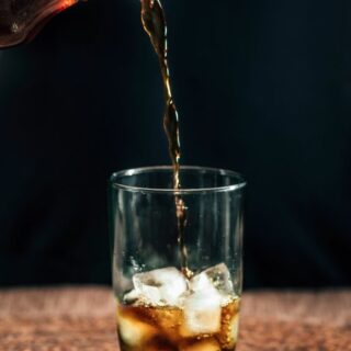 Coffee being poured into a clear glass with ice cubes.