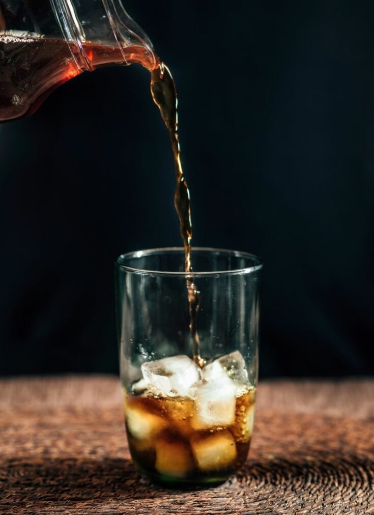 Coffee being poured into a clear glass with ice cubes.